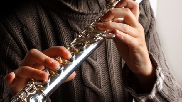A musician pressing keys on a flute with detailed focus on the hands and instrument