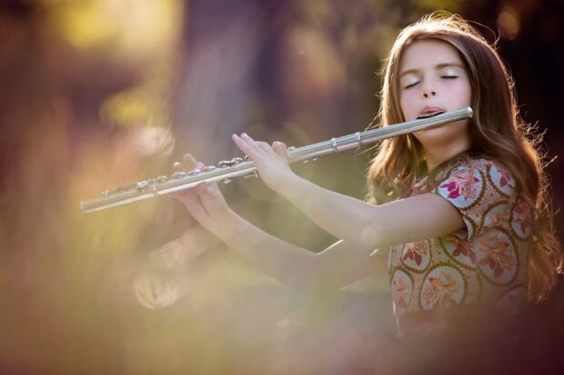 Young girl playing flute with closed eyes in a soft glowing natural setting