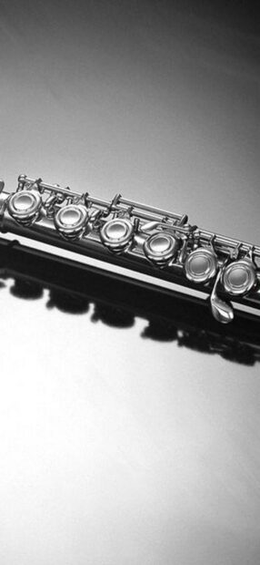 A close up of a flute showing its keys and reflecting on a smooth surface