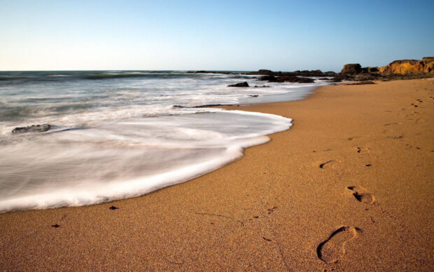 Footprints in the sand along the beach near the ocean waves