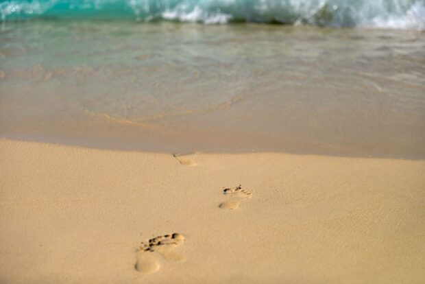 Footprints in the sand along the beach with waves in the background