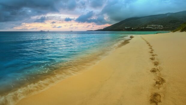 Footprints in the sand along the shoreline during a colorful sunset