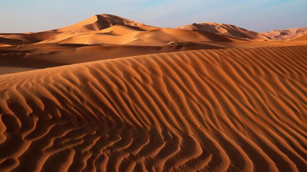 A trail of footprints in the sand crossing the desert dunes under clear blue sky