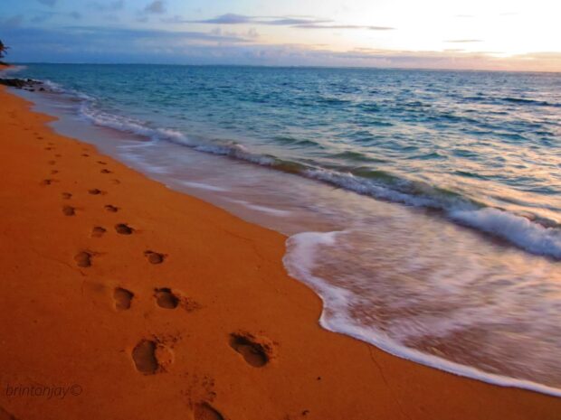 Footprints in the sand along the beach shore with waves approaching at sunset