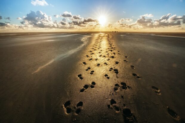 Footprints in the sand leading towards the sunset on a vast beach