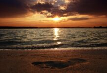 A footprint on the sand at sunset with waves and a glowing sky in the background