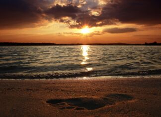 A footprint on the sand at sunset with waves and a glowing sky in the background