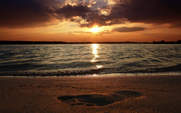 A footprint on the sand at sunset with waves and a glowing sky in the background