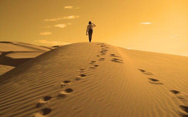 A person walking on sand dunes leaving footprints in the sand at sunset