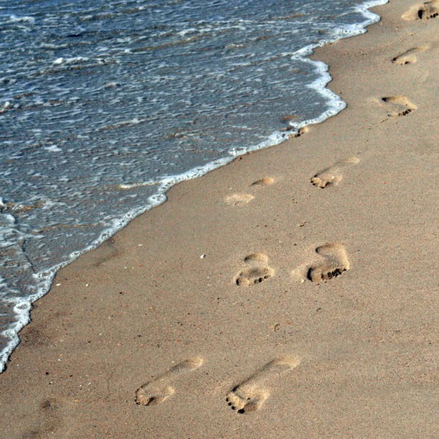 Footprints in the sand along the shoreline with waves approaching the beach