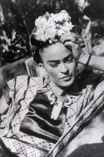 Frida Kahlo wearing traditional clothing and floral headpiece resting her head on her hand