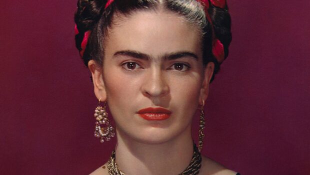 Close up portrait of Frida Kahlo with traditional earrings and hairstyle on red background