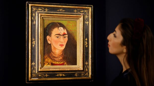 A woman observing a detailed Frida Kahlo painting in an ornate frame