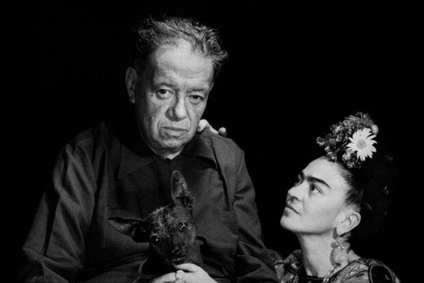 Frida Kahlo looking at a man holding a dog in a black and white portrait