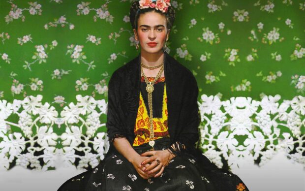 Frida Kahlo sitting in traditional attire with a green floral background
