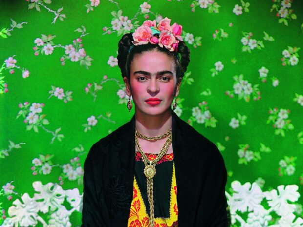 Frida Kahlo wearing floral headpiece and traditional attire against a green floral background