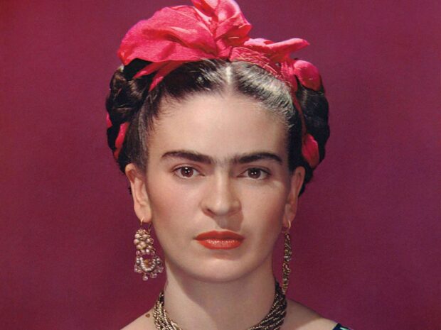 Frida Kahlo portrait with red headband and pearl earrings against a red background