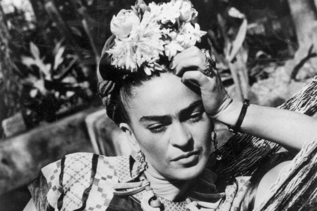 Frida Kahlo resting with flowers in her hair in a black and white portrait