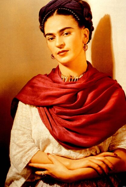 Frida Kahlo wearing a red shawl and white blouse with her arms crossed
