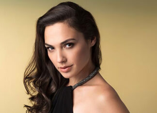 Gal Gadot posing confidently with long dark hair and a black dress against a beige background