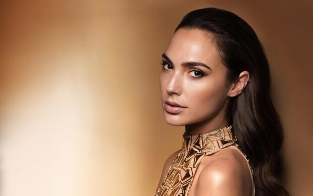 Gal Gadot wearing a stylish gold dress with long dark hair against a warm background