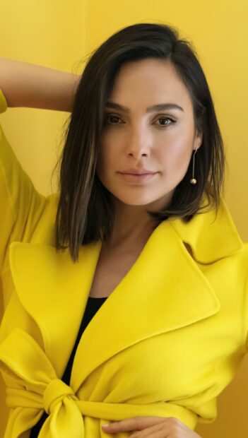 Gal Gadot wearing a bright yellow coat posing with a confident expression against a yellow background