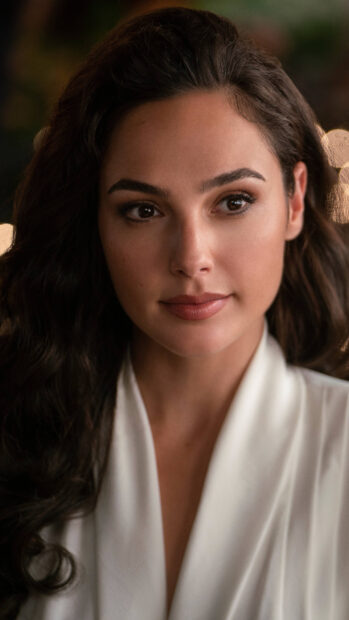 Gal Gadot with long dark hair wearing a white outfit looking thoughtful