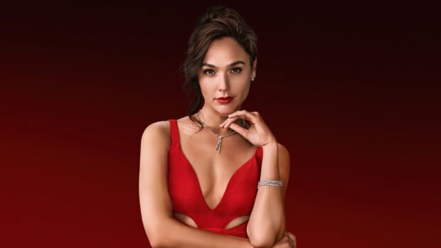 Gal Gadot wearing a red dress and necklace posing confidently against a red background