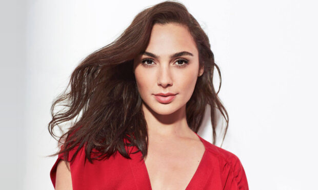 Gal Gadot wearing a red dress with flowing hair against a white background