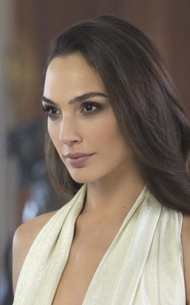 Gal Gadot wearing a shimmering dress and looking thoughtfully in a close up portrait