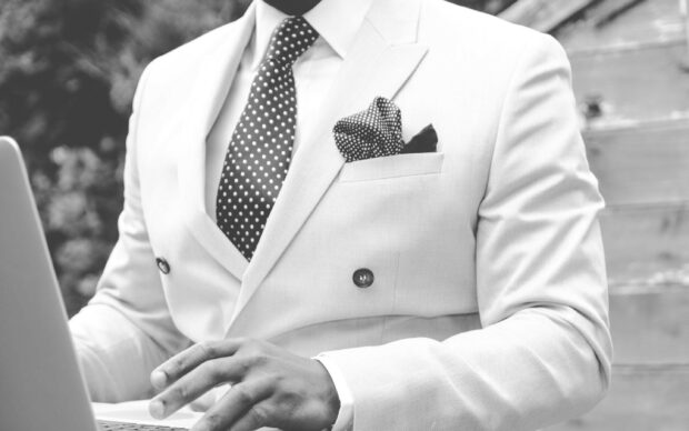 A gentleman wearing a polka dot tie and a suit jacket using a laptop outdoors