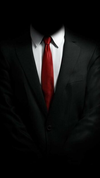 A gentleman wearing a black suit and a red tie with a white shirt in a dark setting