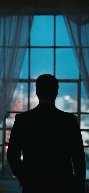 Gentleman silhouette standing in front of a window with city lights outside at dusk