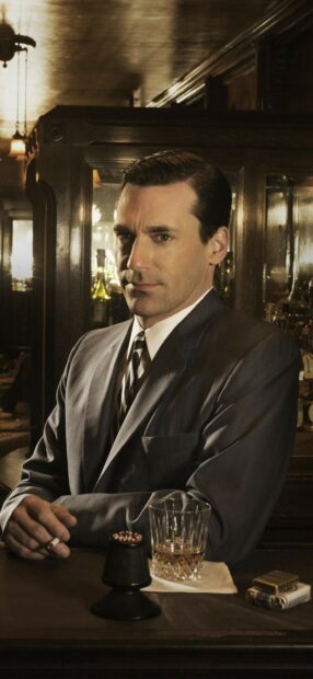 A gentleman in a classic suit sitting at a bar with a drink and cigarette in hand