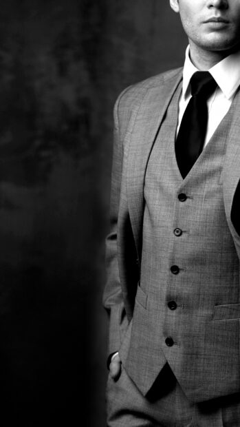 A gentleman wearing a tailored suit and tie standing with his hand in pocket