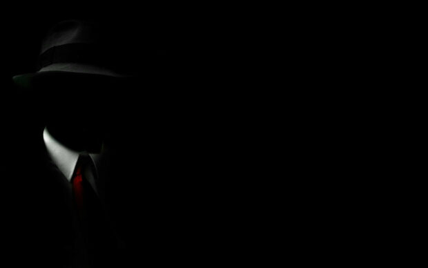 A gentleman wearing a hat and red tie in dark lighting