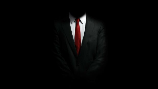 A gentleman wearing a suit and red tie standing in darkness