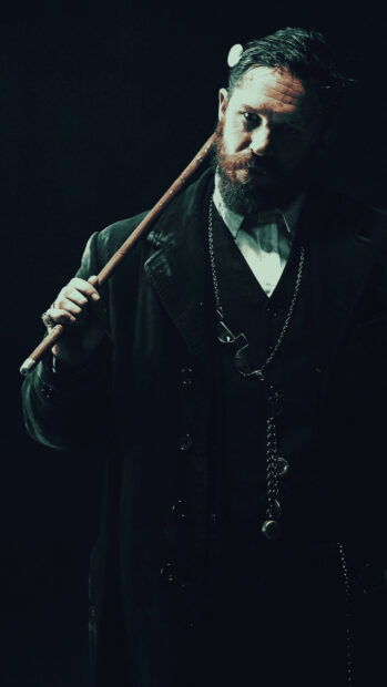 Bearded man with vintage style holding a cane in dark elegant clothing
