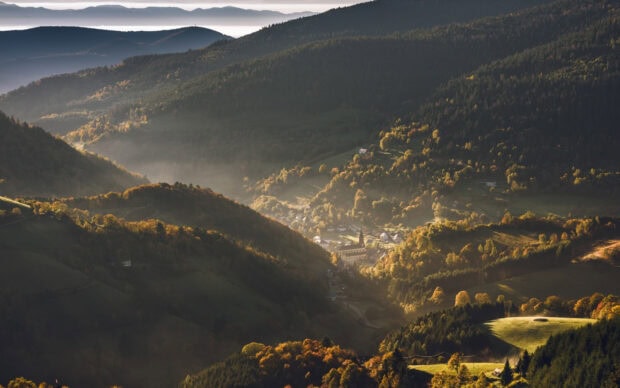 A serene valley with rolling hills and a small village surrounded by forested geography
