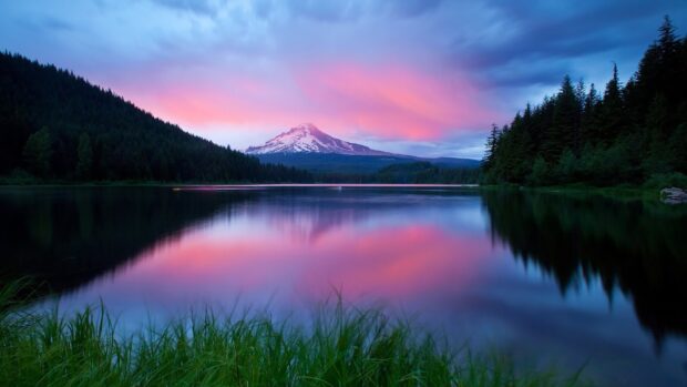 Snow capped mountain with forest and lake reflecting colorful sky at sunset