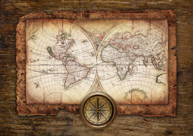 An antique world map with detailed continents and a vintage compass on a wooden surface