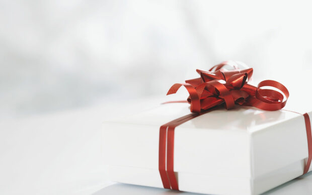 A white gift box wrapped with a shiny red ribbon and bow on a bright surface
