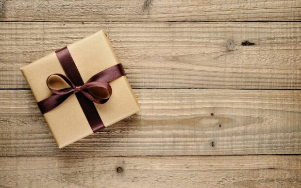 A wrapped gift with a brown ribbon on a wooden surface showing a simple present box