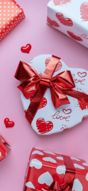 Heart shaped gifts with red ribbons and love designs on a pink background