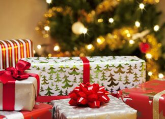 A collection of colorful gifts with red ribbons under a glowing Christmas tree decorated with lights