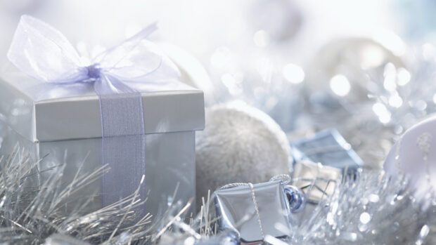 A silver gift wrapped with a ribbon surrounded by festive decorations and holiday gifts