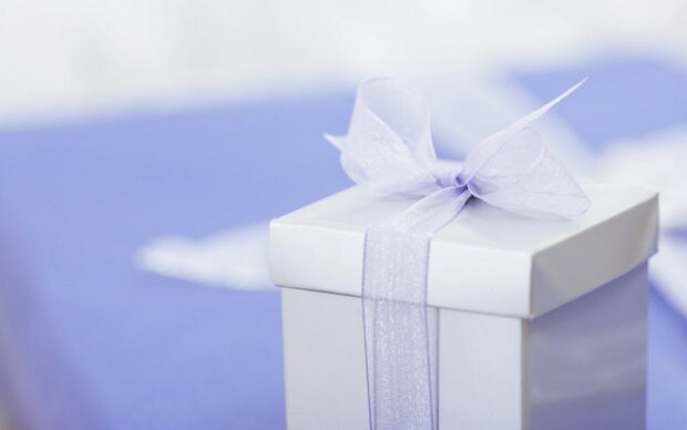 A white gift box with a sheer ribbon bow sitting on a purple surface with gifts
