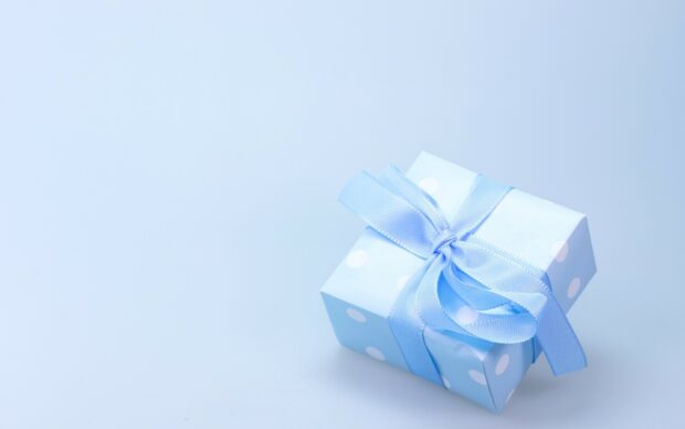 A small gift wrapped with blue ribbon is placed on a light blue surface