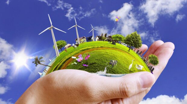 A hand holding a vibrant green environment with trees animals and wind turbines