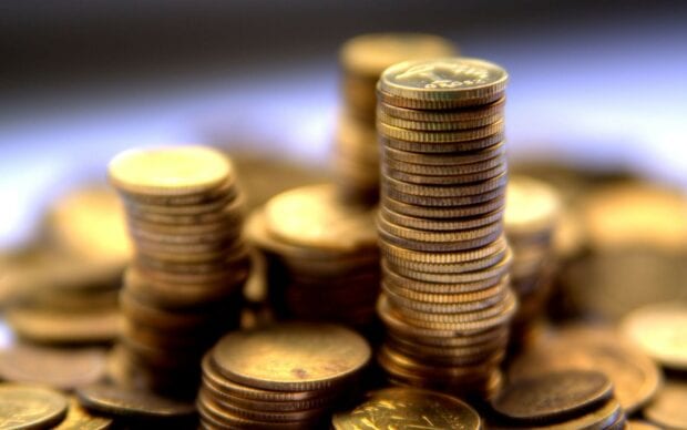 A close up view of stacked gold coins with a blurred background showing gold coins